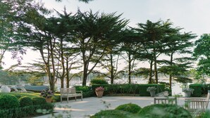 A serene outdoor seating area with benches and potted plants, surrounded by lush greenery and trees. - Villa Tri Men (Combrit)