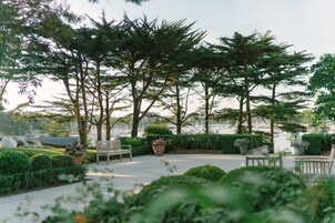 Un espacio al aire libre tranquilo con bancos y plantas en macetas, rodeado de abundante follaje y árboles.