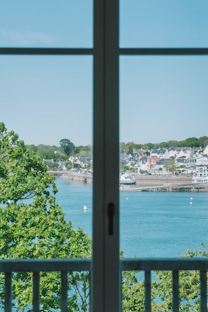 A coastal town with buildings along the waterfront, a clear sky, and a view through a window with a visible lock on the side. - Villa Tri Men (Combrit)