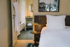 A hotel room with a bed, a bedside table with a lamp, a bathroom with a sink and toilet, and a framed picture on the wall.