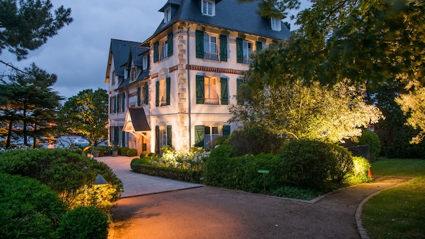 A large, multi-story building with a traditional architectural style, featuring a prominent entrance and a well-maintained garden area. - Villa Tri Men (Combrit)