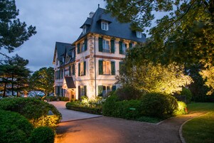 Un edificio grande de varios pisos con estilo arquitectónico tradicional, que destaca por su entrada principal y un jardín bien cuidado.