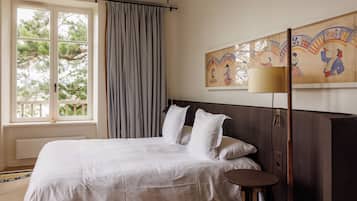 A bedroom with a large bed, a bedside table, a lamp, and a window with curtains.