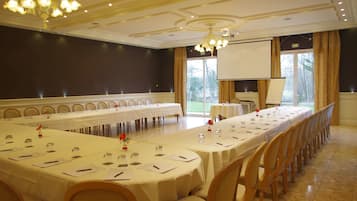 Un salón de conferencias con una larga mesa, sillas, una pantalla de proyector y un amplio ventanal con cortinas.