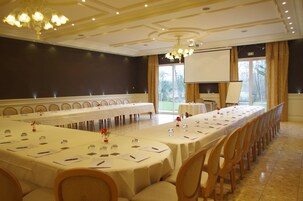 Un salón de conferencias con una larga mesa, sillas, una pantalla de proyector y un amplio ventanal con cortinas.
