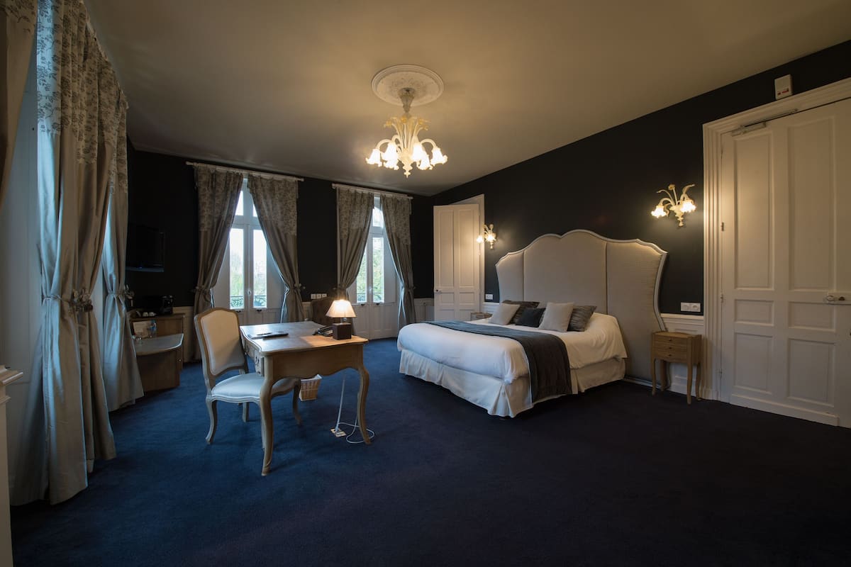 Una habitación de hotel con una cama grande, un escritorio con lámpara, una silla y un armario.