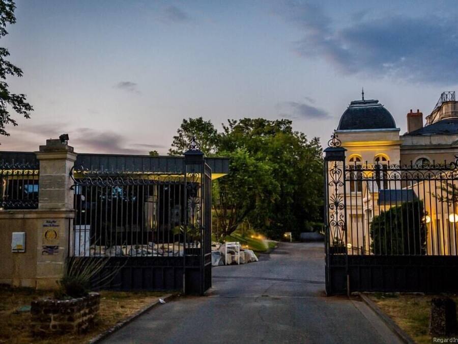 A gated entrance with a metal gate and a building with a dome and arched windows in the background.