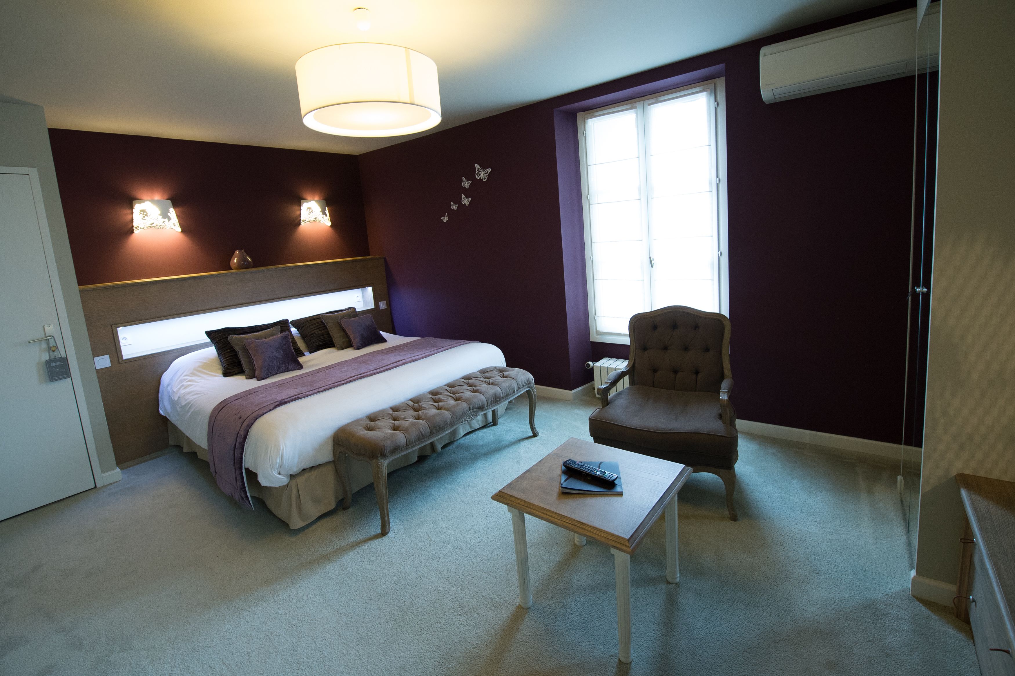 A bedroom with a bed, a bench, a chair, a table, and a window.