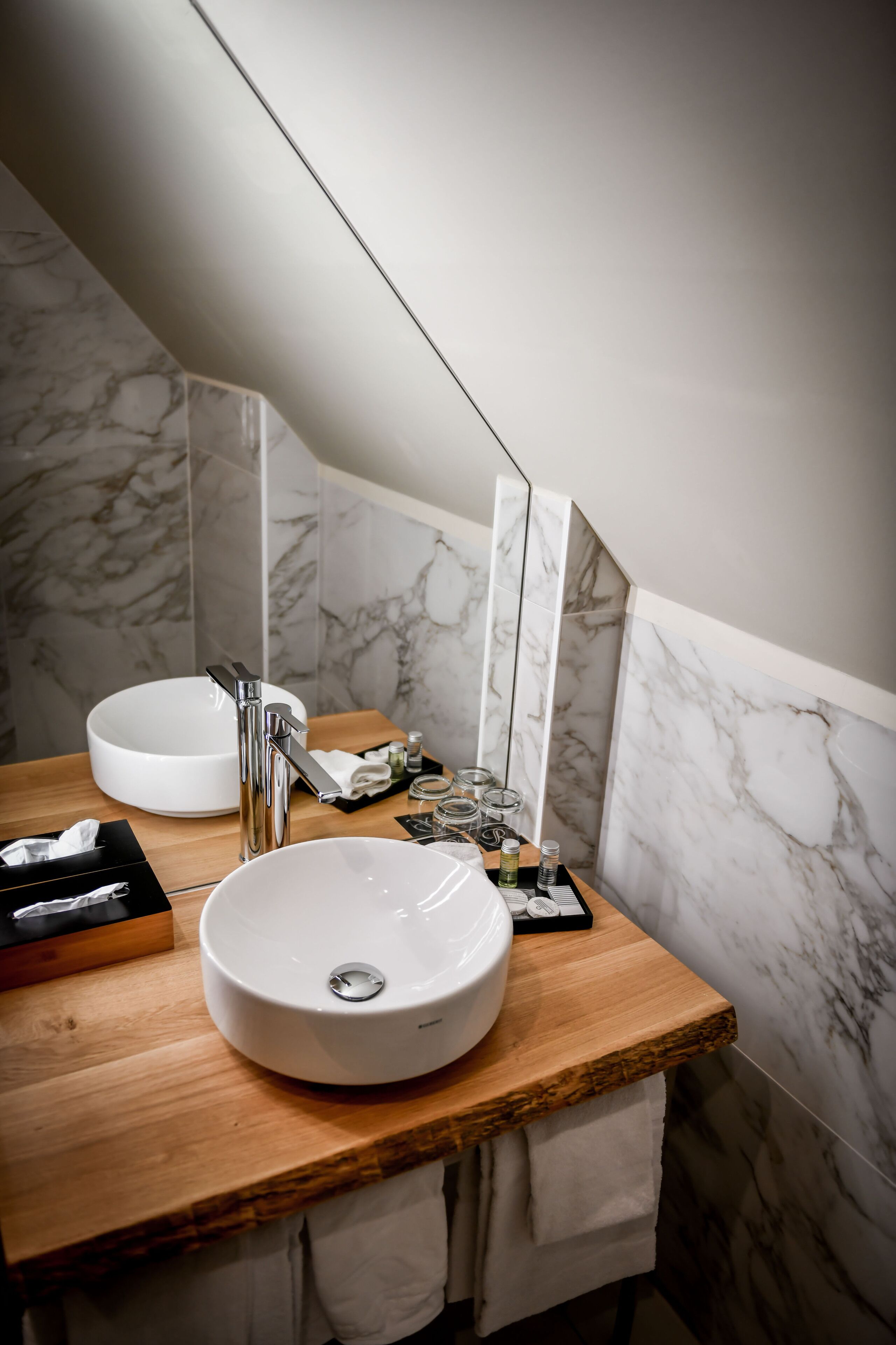A modern bathroom with a wooden vanity, two sinks, and marble walls.