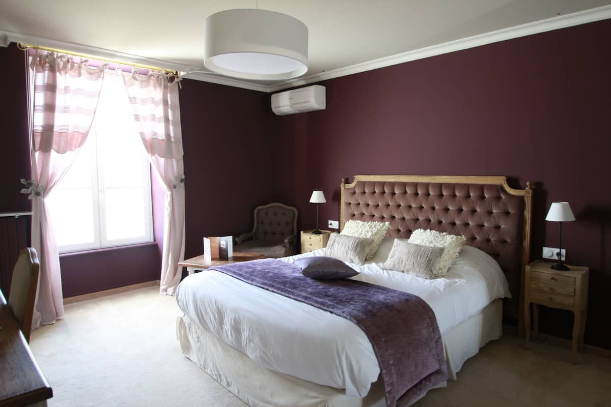 Un dormitorio con una cama grande, dos mesitas de noche con lámparas, una silla y una ventana con cortinas.