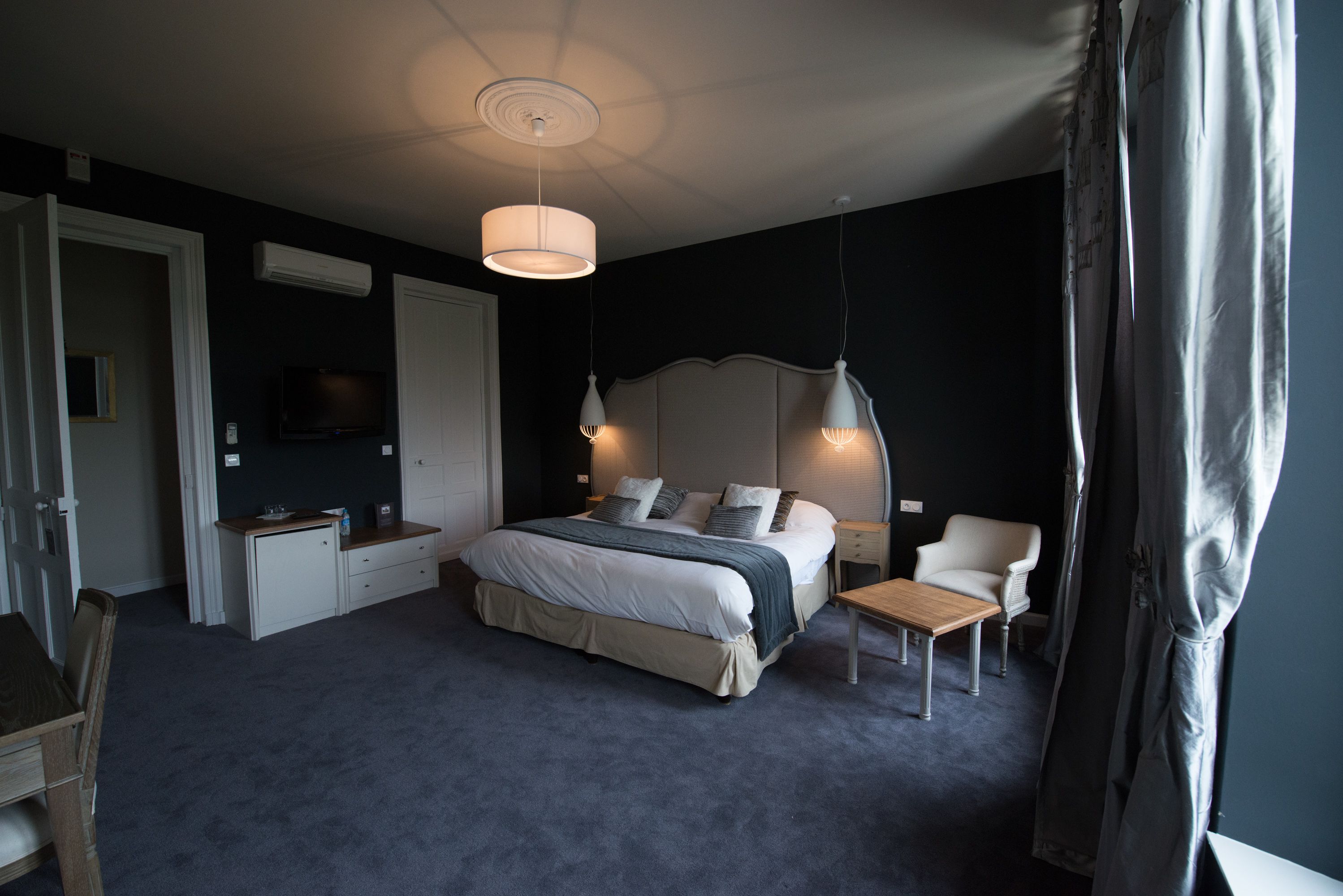 A bedroom with a large bed, bedside tables, a chair, a desk, and a television.