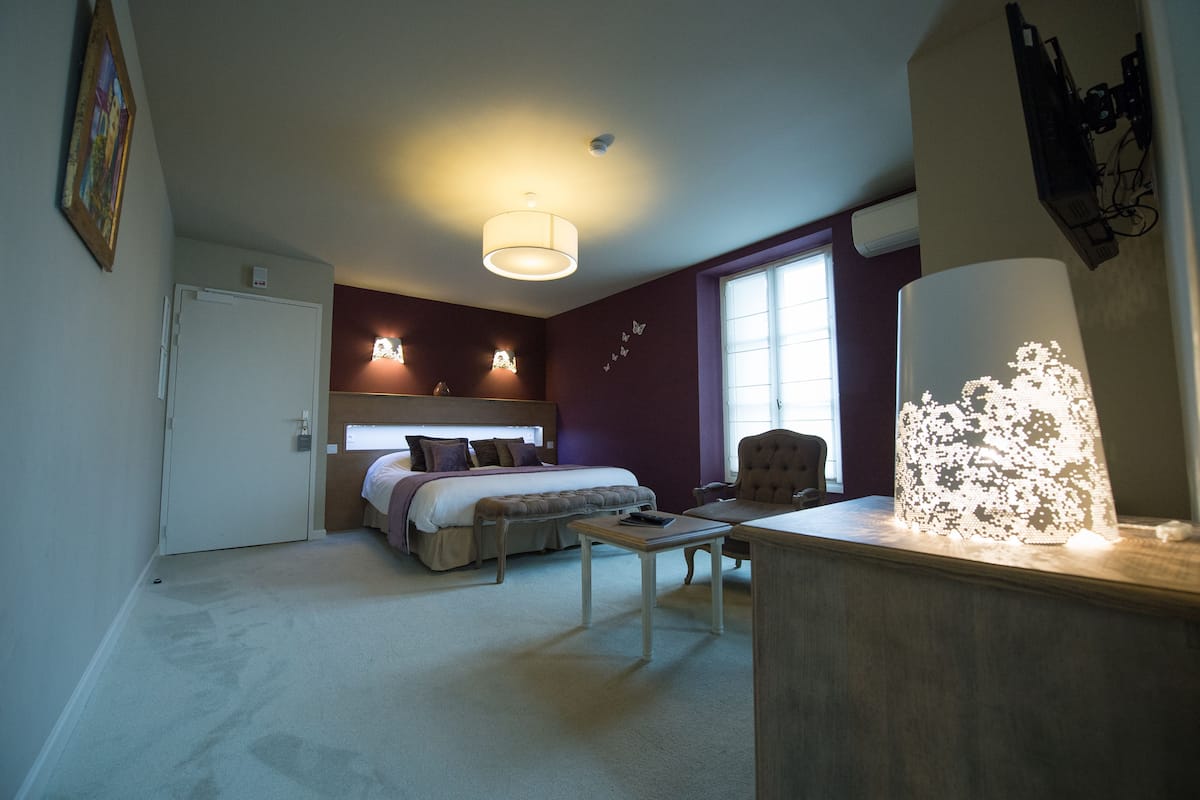 Un dormitorio con cama, mesitas de noche, escritorio, silla, lámpara y ventana.