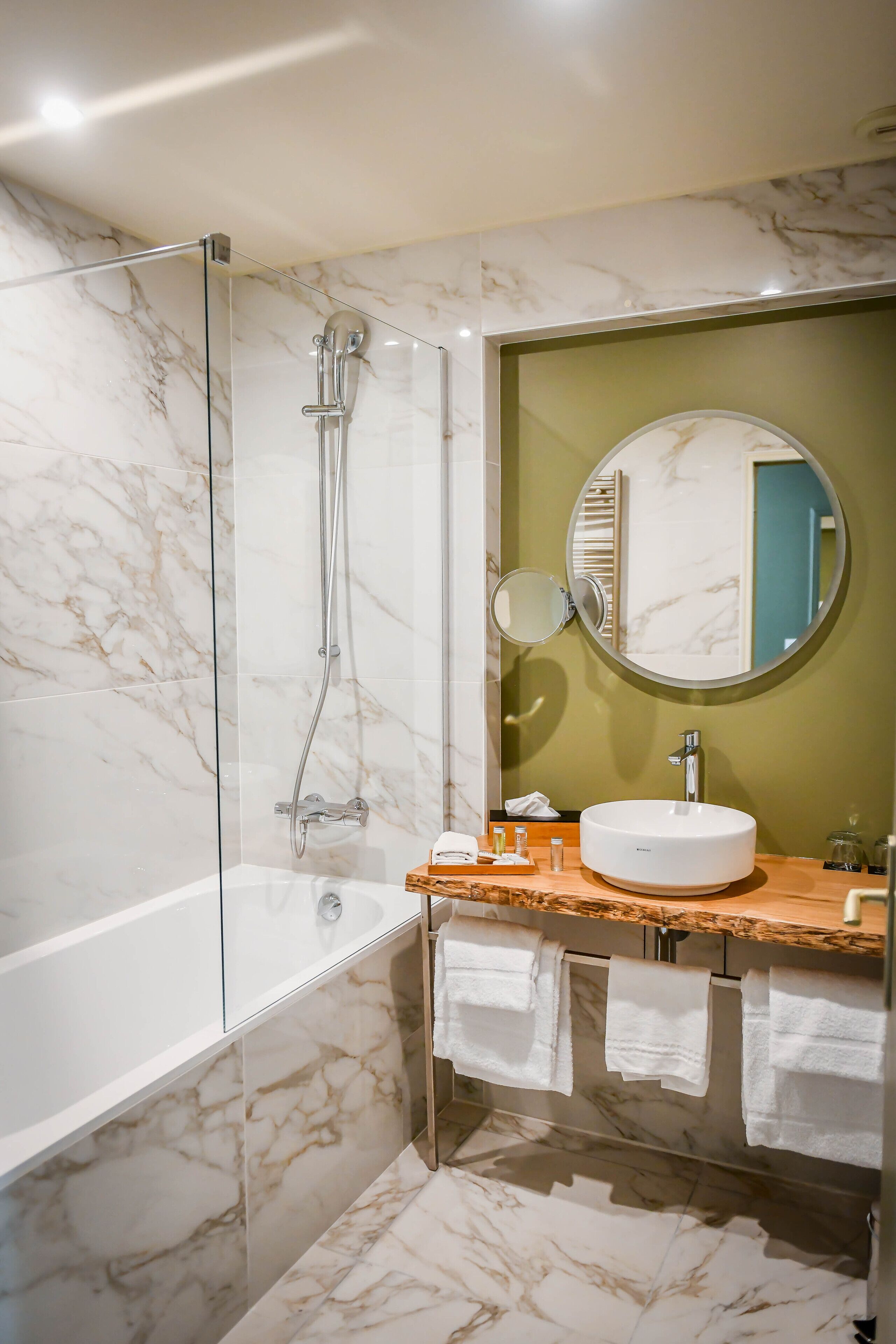 Een badkamer met een douche met glazen wand, een ronde spiegel en een vloer van marmeren tegels.