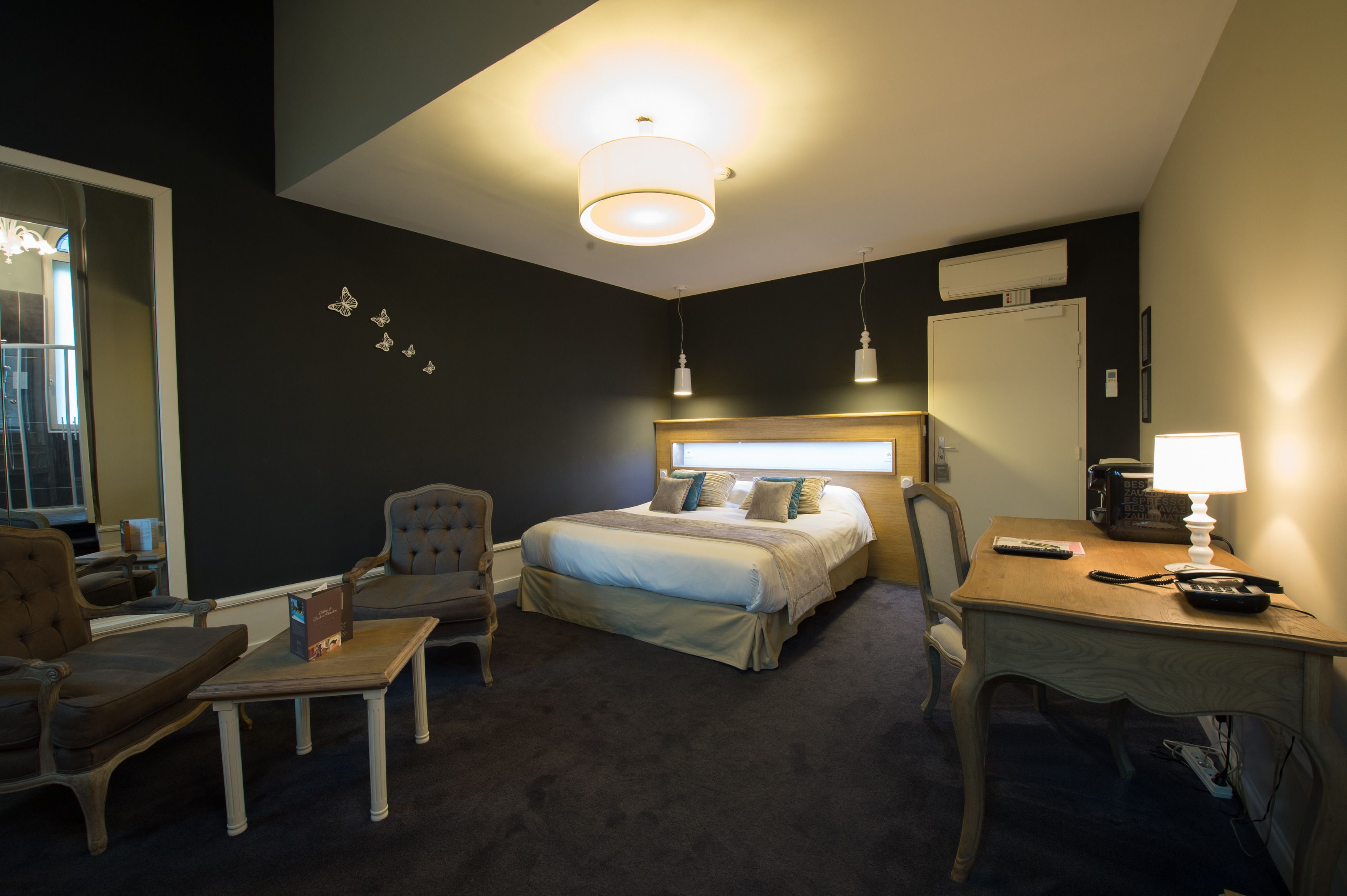 A hotel room with a bed, a desk, a chair, a lamp, and a mirror.