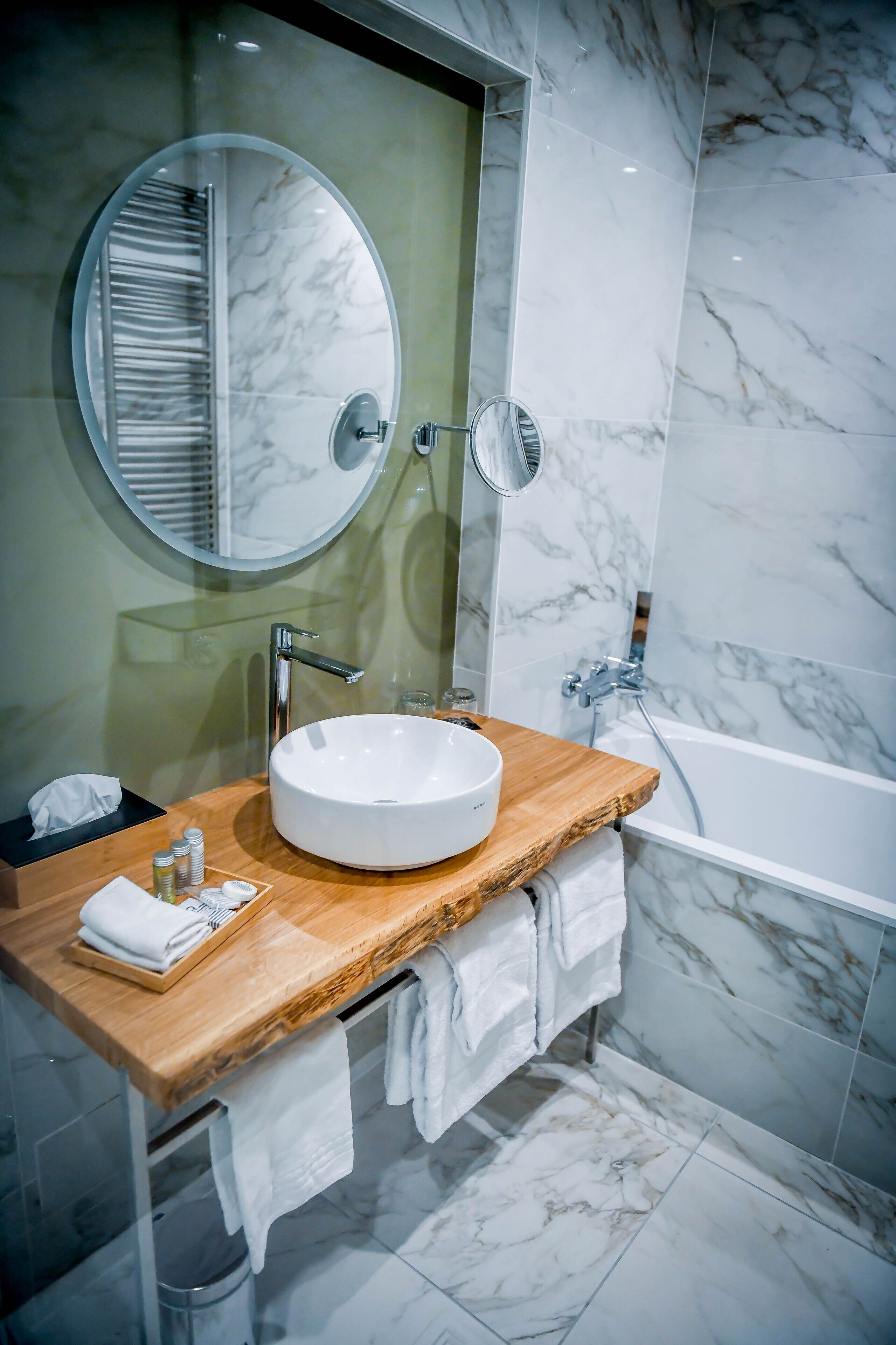 A modern bathroom with a large oval sink, a wooden countertop, a round mirror, and a bathtub.