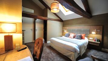 A bedroom with a large bed, a desk, a chair, and a bedside table with a lamp.