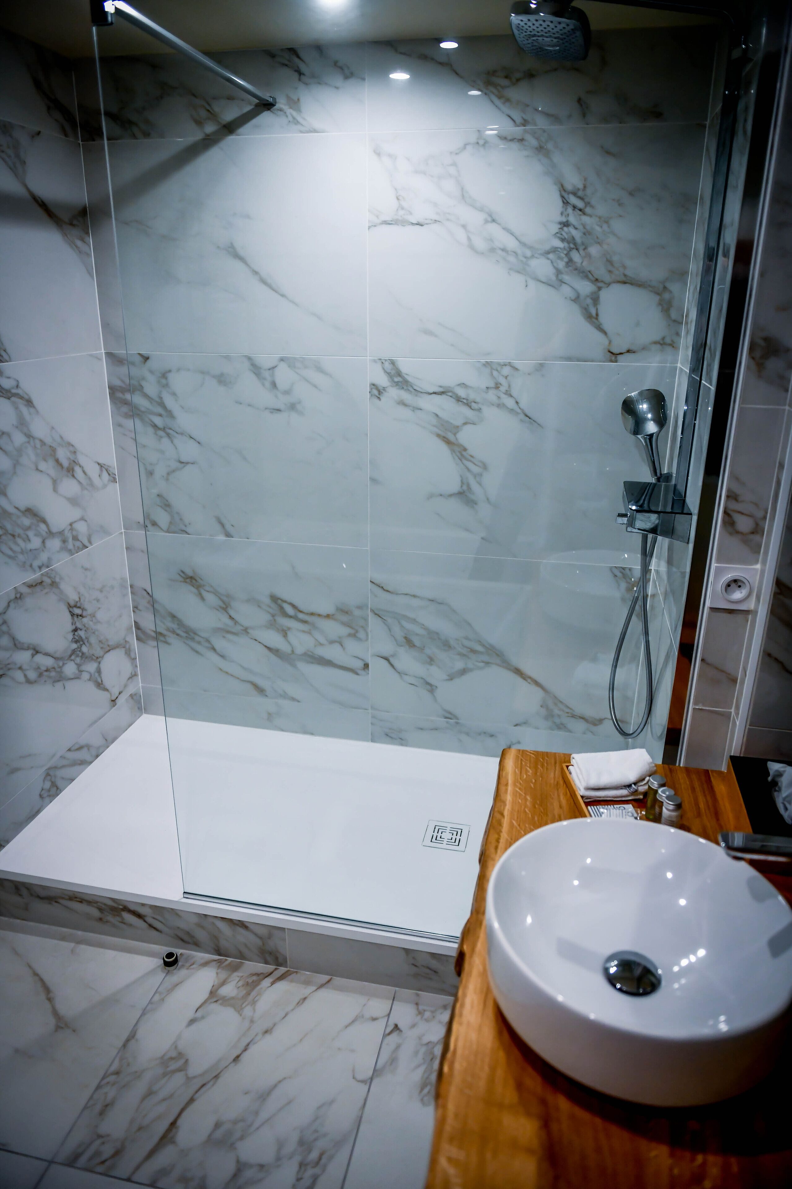 A modern bathroom with a glass shower enclosure, marble tiles, and a wooden vanity with a sink.