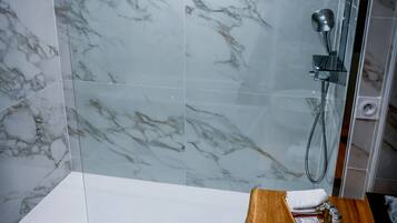 A modern bathroom with a glass shower enclosure, marble tiles, and a wooden vanity with a sink.