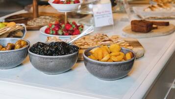Un buffet proposant une variété d’aliments, notamment des fruits, des pâtisseries, ainsi qu’un panneau indiquant les boissons disponibles.