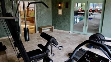 Un gimnasio con equipo de ejercicio, una banca y vistas a un área exterior con sillas y una piscina.