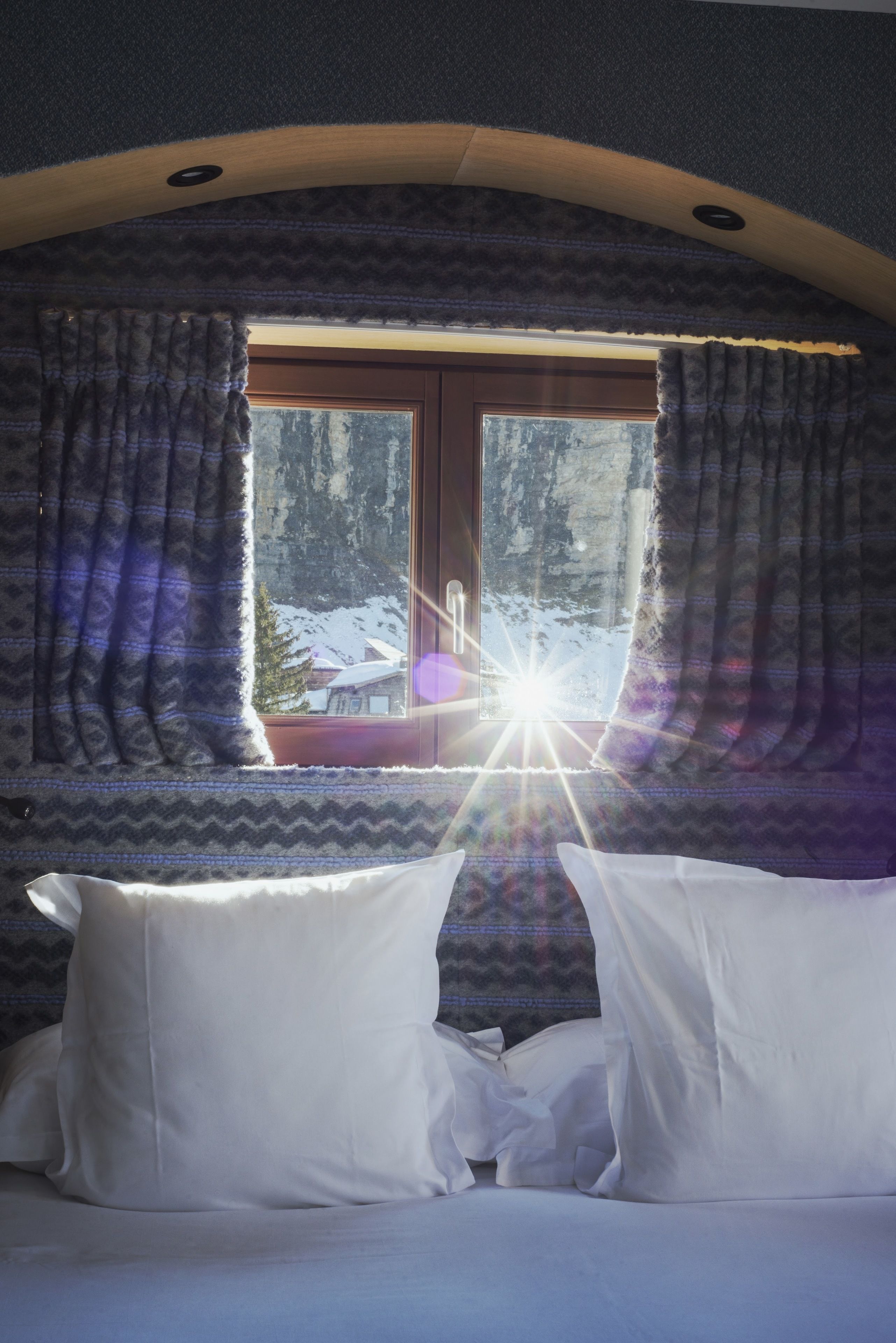 A bedroom with a bed, white pillows, and a window with curtains.
