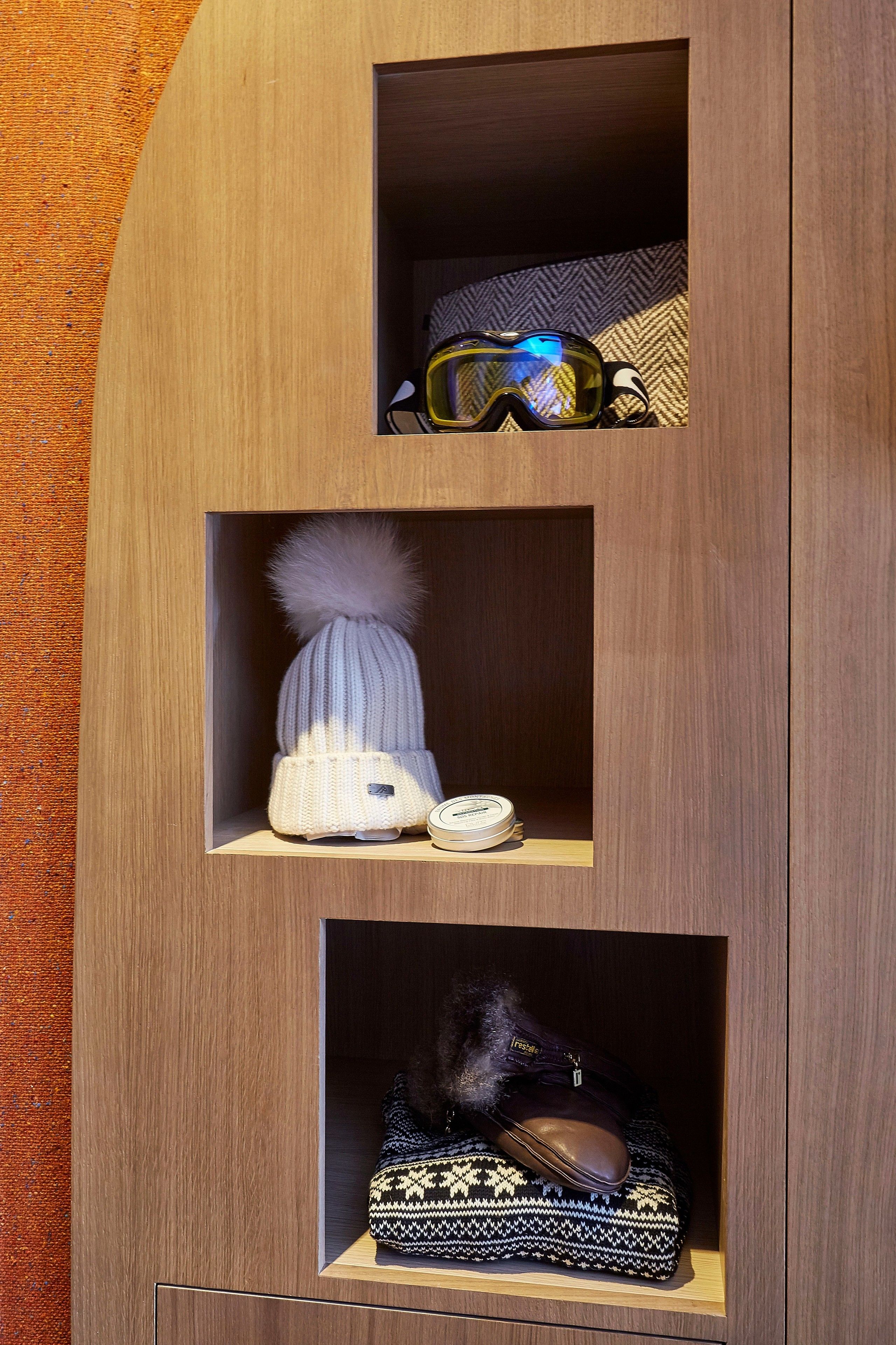 Une armoire en bois avec trois étagères, chacune contenant différents articles : une paire de lunettes de protection, un bonnet en tricot et un sac à motifs.