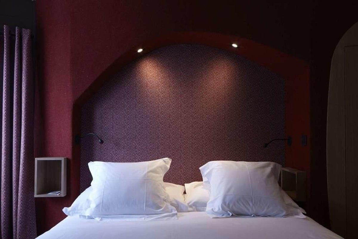Habitación de hotel con una cama grande, cabecera con textura y una mesita de noche pequeña.