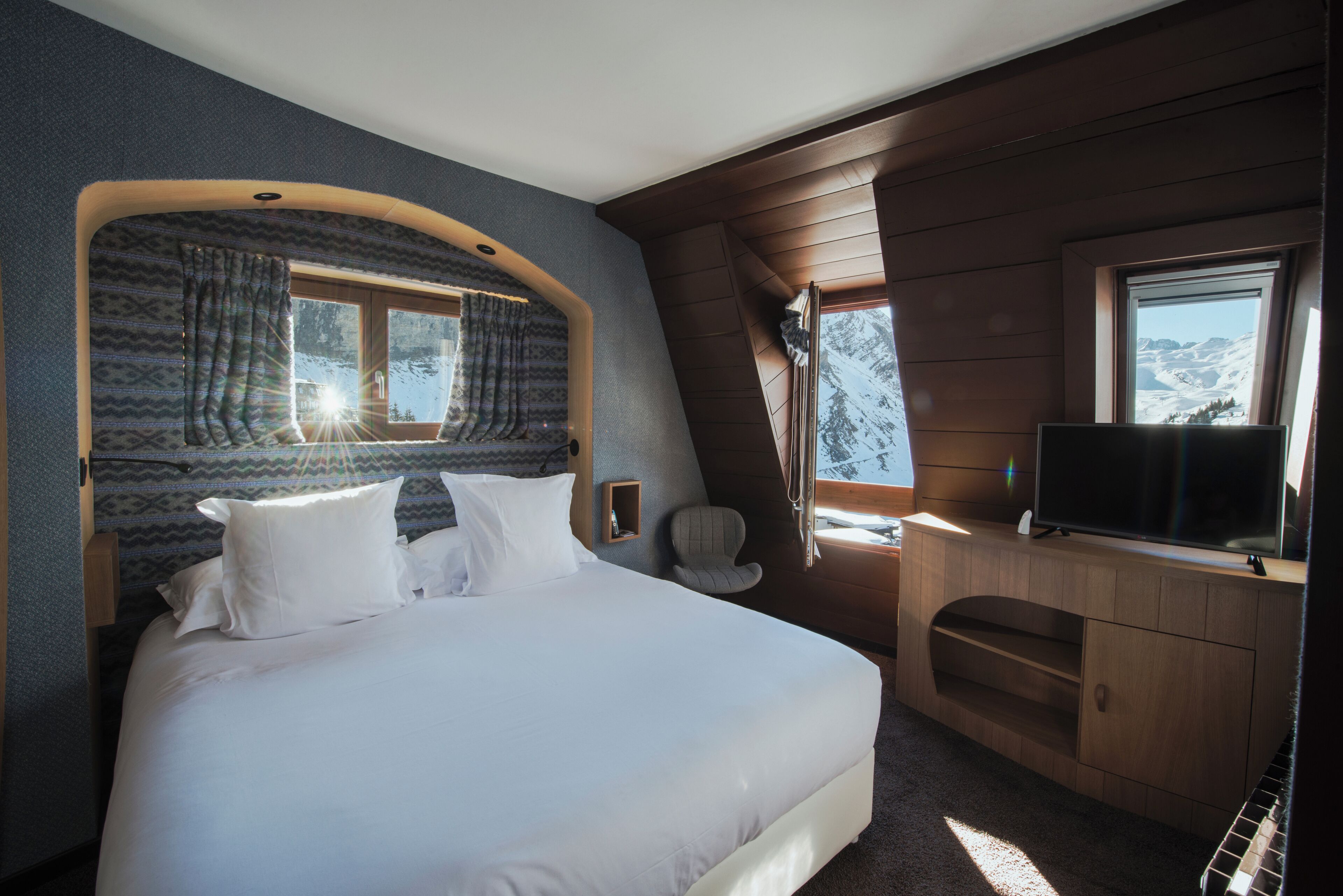 Een slaapkamer met een groot bed, een televisie, een stoel en een raam met uitzicht op de bergen.