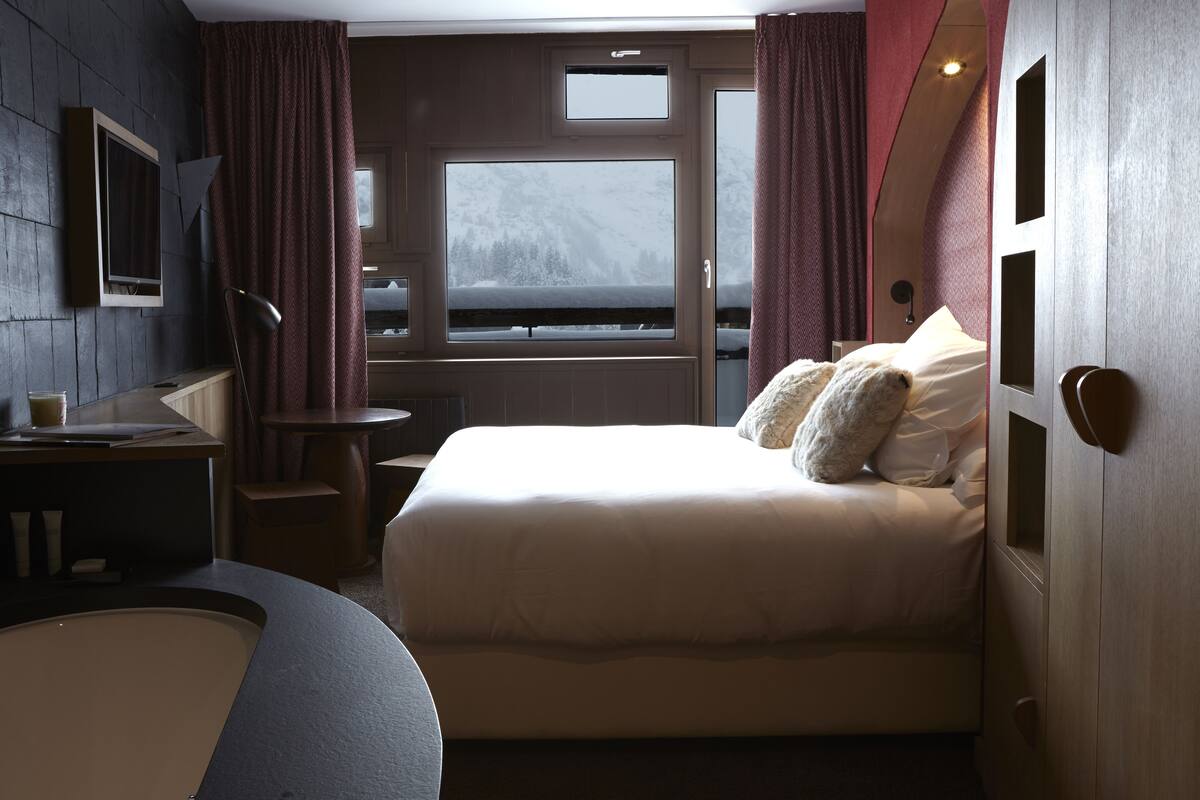 Una habitación de hotel moderna con una cama, un escritorio y una ventana con vistas a un paisaje nevado.