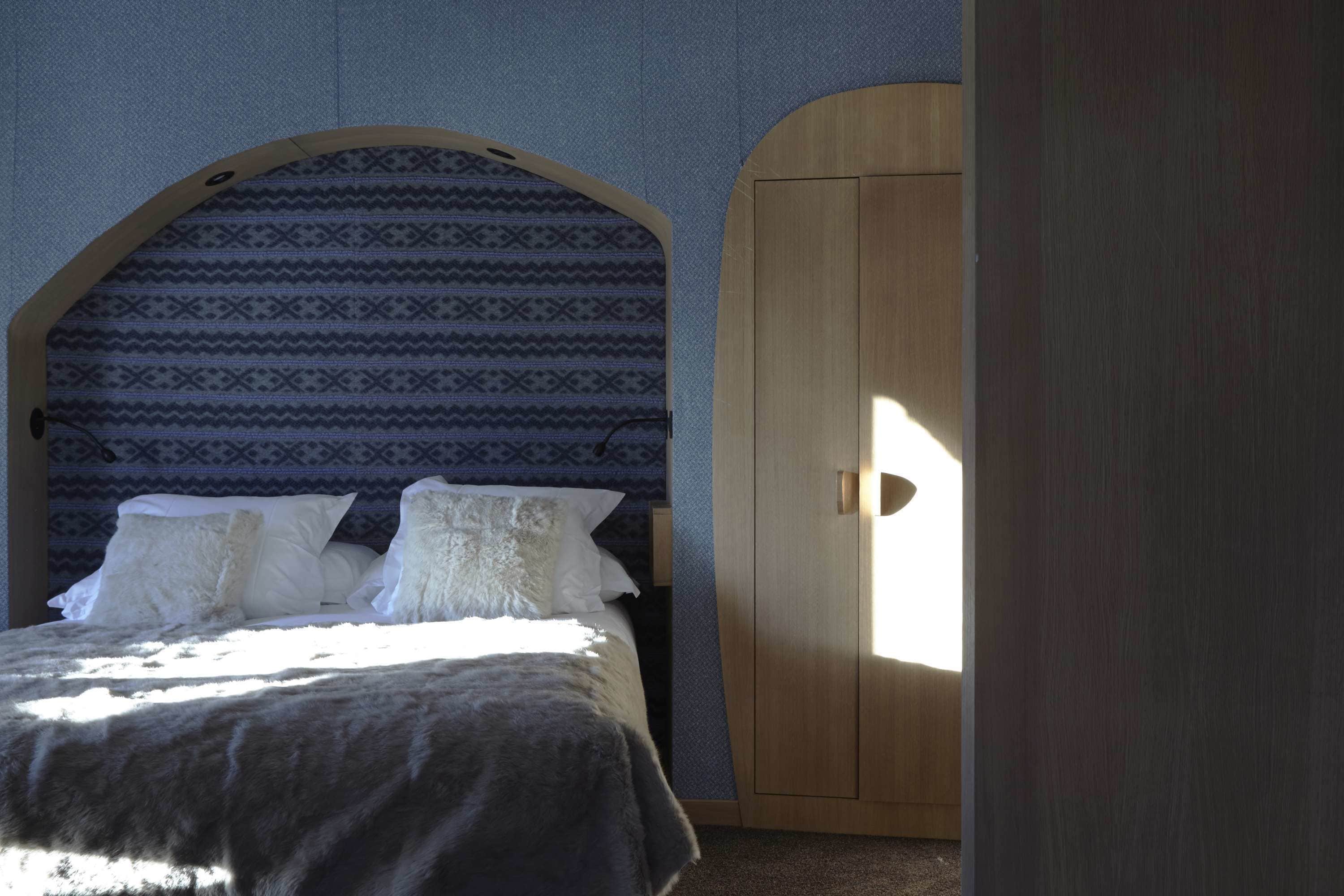 A bedroom with a bed, patterned wallpaper, and a wooden wardrobe.