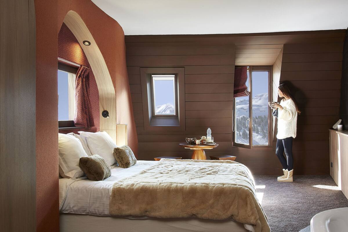 Un dormitorio con una cama grande, una mesita pequeña y una ventana con vistas a la montaña.