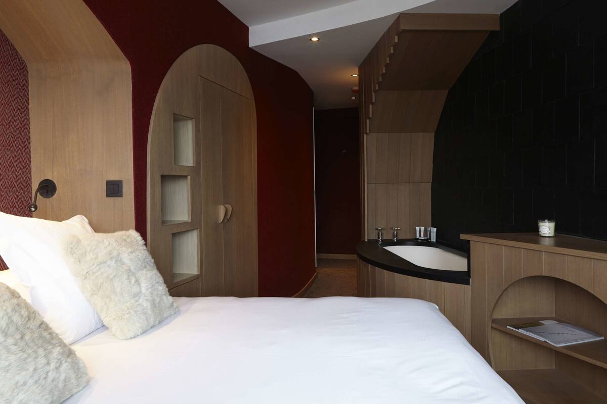 Una habitación de hotel moderna con una cama grande, un tocador de madera con un lavabo y un espejo.