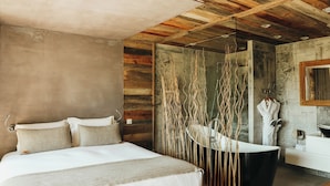 A modern bedroom with a large bed, a black bathtub, and a wooden ceiling.