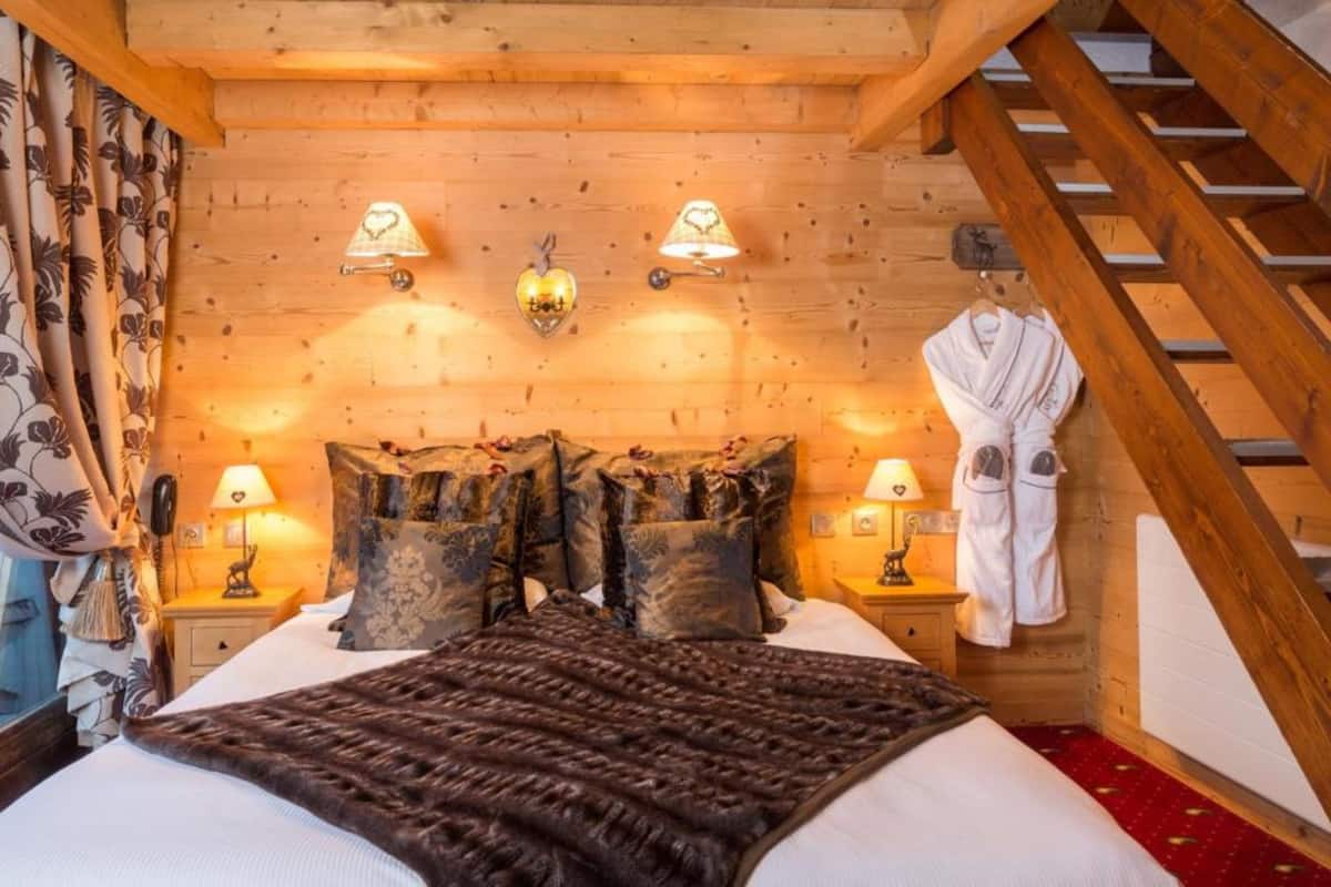 Ein gemütliches Schlafzimmer aus Holz mit einem Bett, zwei Nachttischlampen, einem aufhängbaren Bademantel und einer Holztreppe.