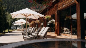 A wooden cabin with a pool area, lounge chairs, and umbrellas.