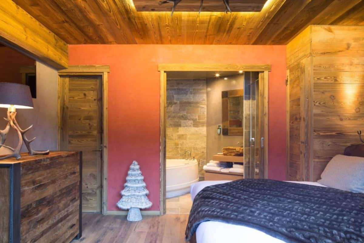 Ein Schlafzimmer mit Holzboden, einem Bett, einem Nachttisch mit Lampe, einer kleinen Weihnachtstanne und einem Badezimmer mit Steinwand und Badewanne.