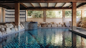 An indoor swimming pool with mosaic tiles, wooden beams, and stone walls.
