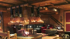 A cozy log cabin interior with a central fireplace, leather furniture, and rustic decor.