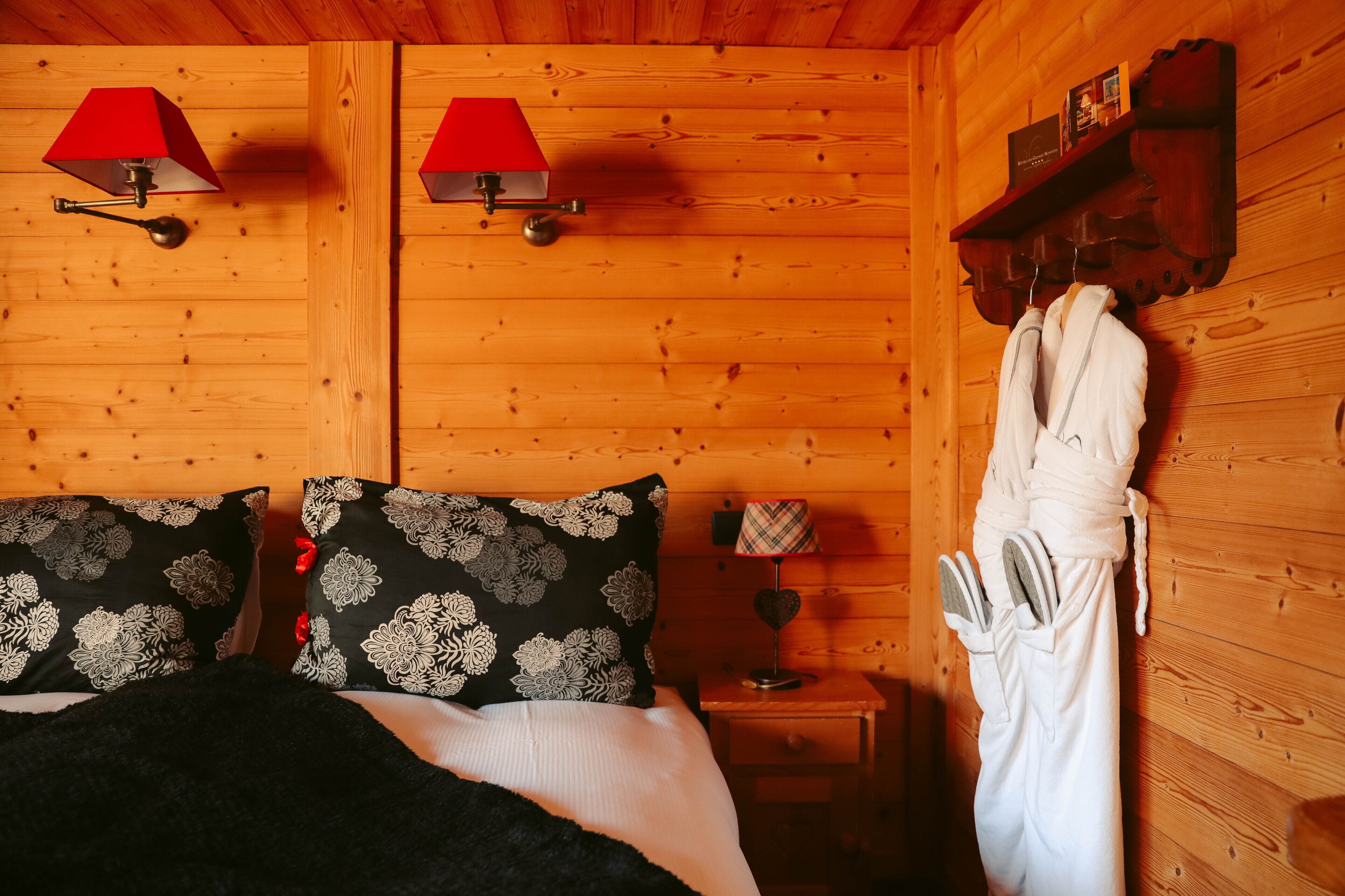 Een houten kamer met twee bedden, een nachtkastje met een lamp, en een badjas die aan de muur hangt.