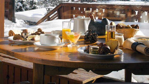 Una mesa de desayuno con vista a la montaña, incluyendo casas cubiertas de nieve y una zona boscosa.