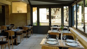 A restaurant with tables set for dining, chairs, and a view through large windows. - Hôtel Belesso (Fontvieille)