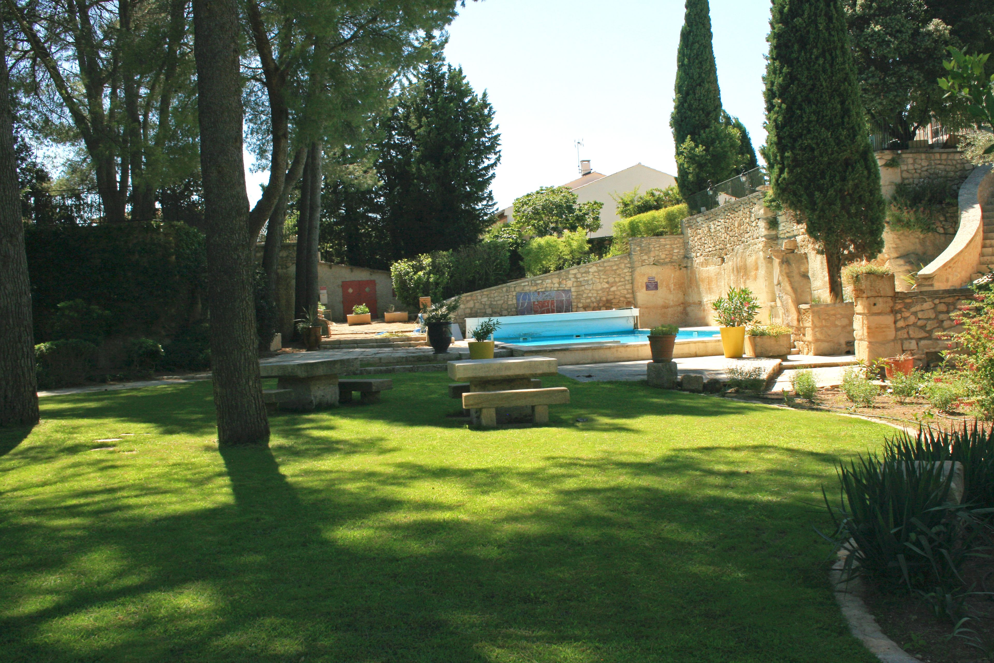 Un área de piscina con pared de piedra, bancos y plantas en macetas.