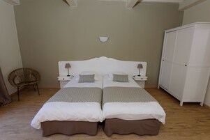 Una cama doble con dos mesitas de noche, una lámpara de pared, un armario y una silla de mimbre.