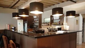 A bar area with a wooden counter, hanging pendant lights, and a bar stocked with bottles. - Hôtel Belesso (Fontvieille)