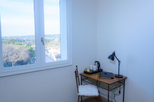 Habitación de esquina con escritorio, silla y vista a un árbol y edificios.