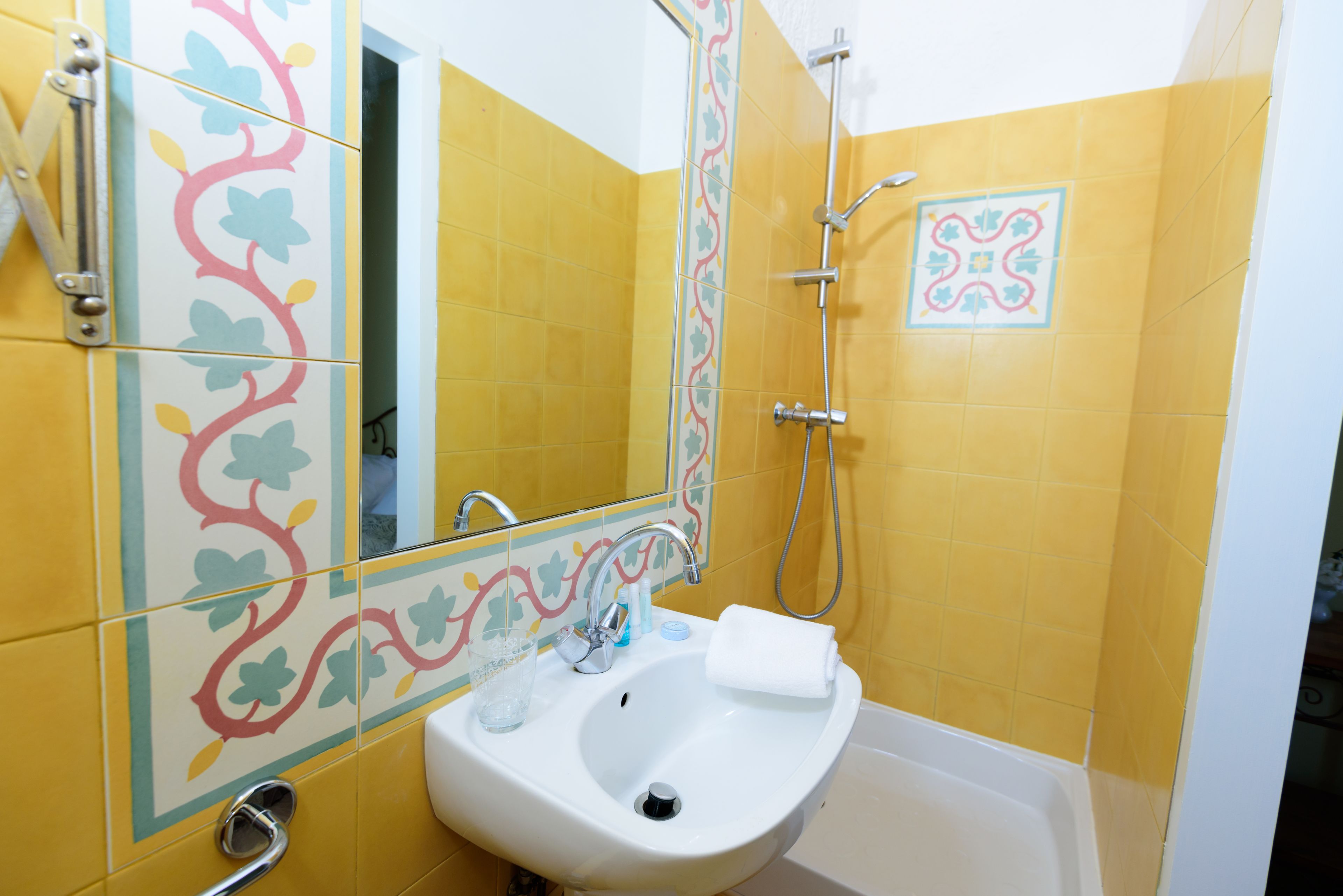 Un baño con paredes de azulejos amarillos, un lavamanos blanco, un espejo y una ducha.