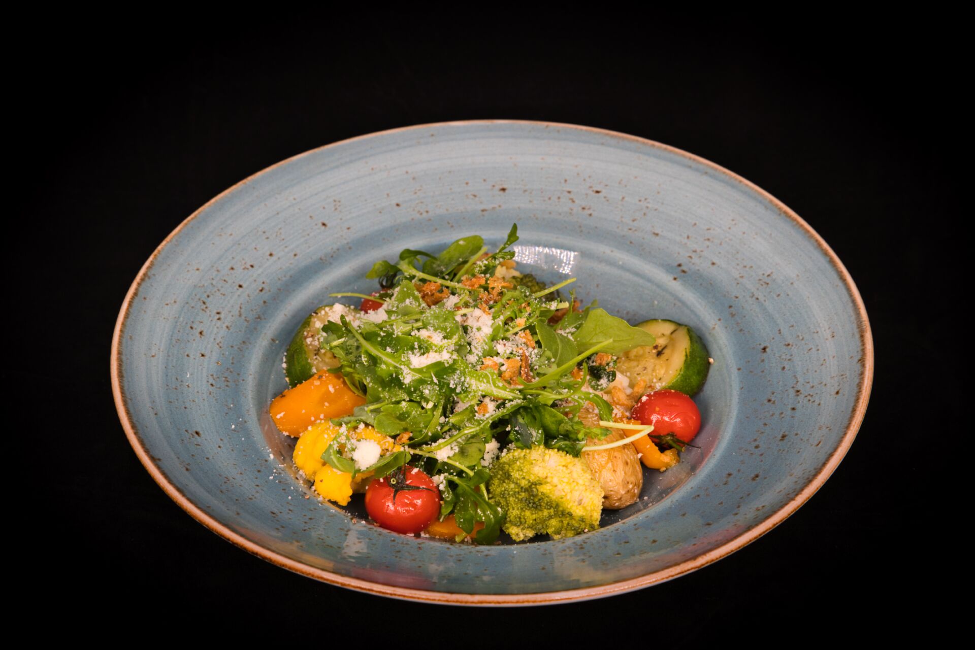 A plate of food with various vegetables and a blue rimmed bowl.