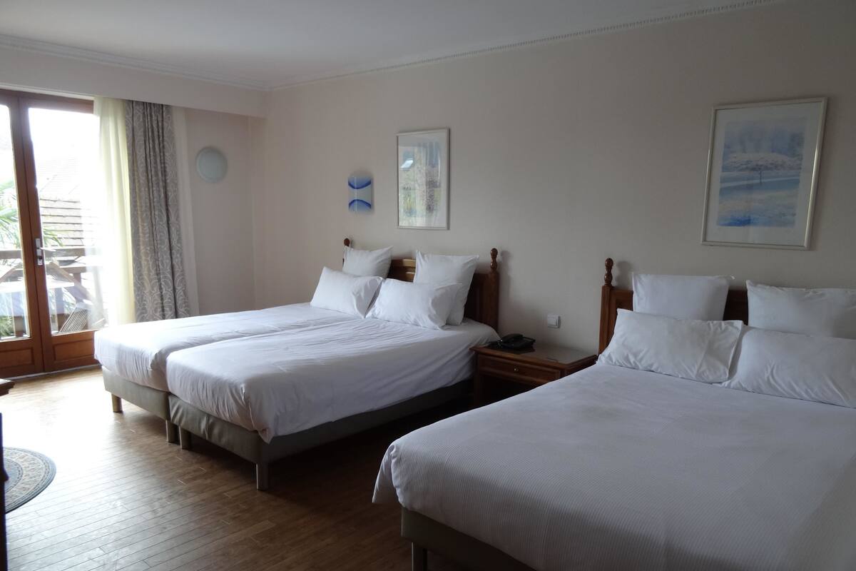 Ein Hotelzimmer mit zwei Einzelbetten, Holzboden, einem kleinen Tisch und Blick ins Freie durch eine Schiebetür.