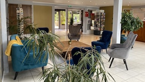 Een ruime lobby met een houten salontafel, blauwe en grijze fauteuils en een boekenkast vol boeken.