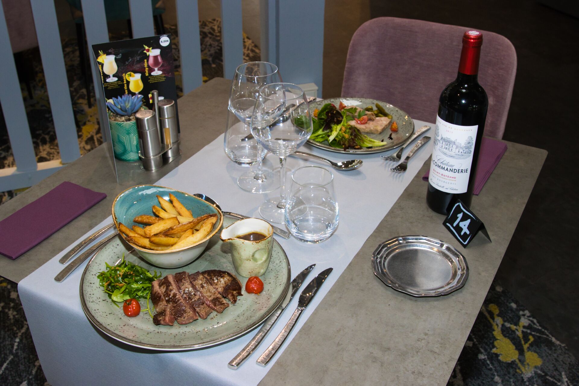 A table set for a meal with plates of food, a bottle of wine, and various glasses.